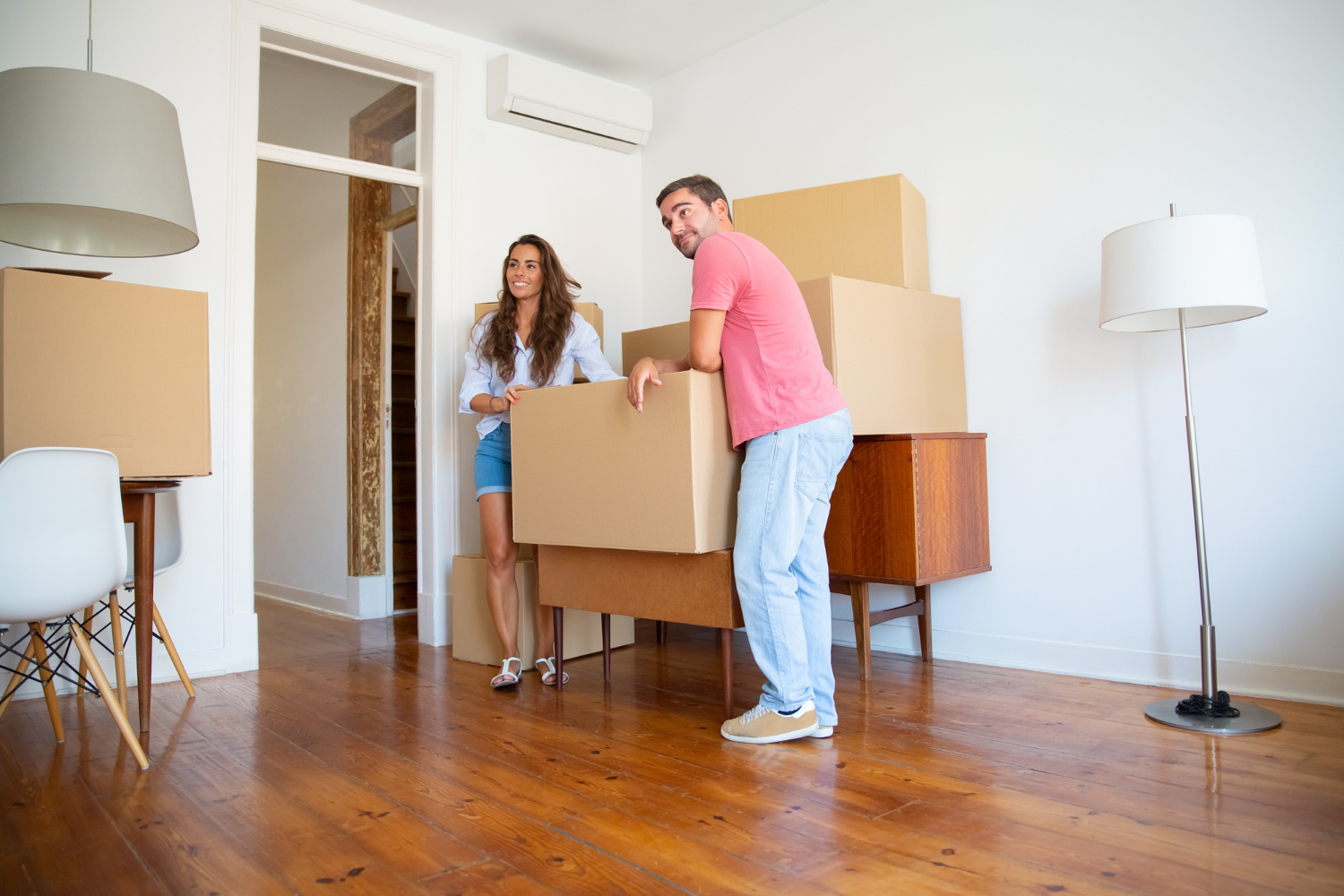 positive-young-couple-looking-their-new-apartment-while-standing-leaning-cardboard-boxes-furniture-indoors
